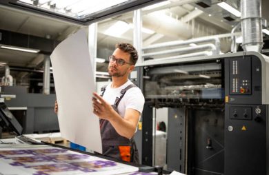 Print shop worker checking quality of imprint and controlling printing process.